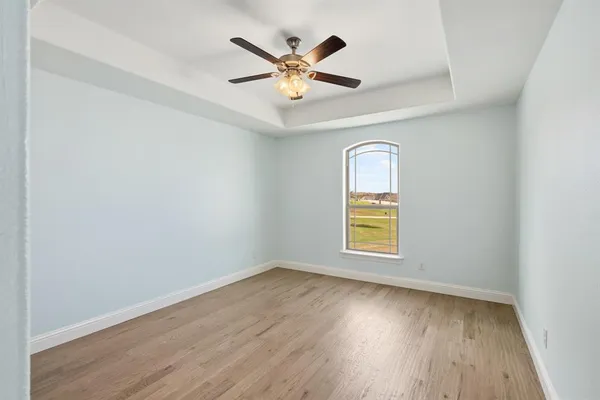 an empty room with wooden floor chandelier fan and windows