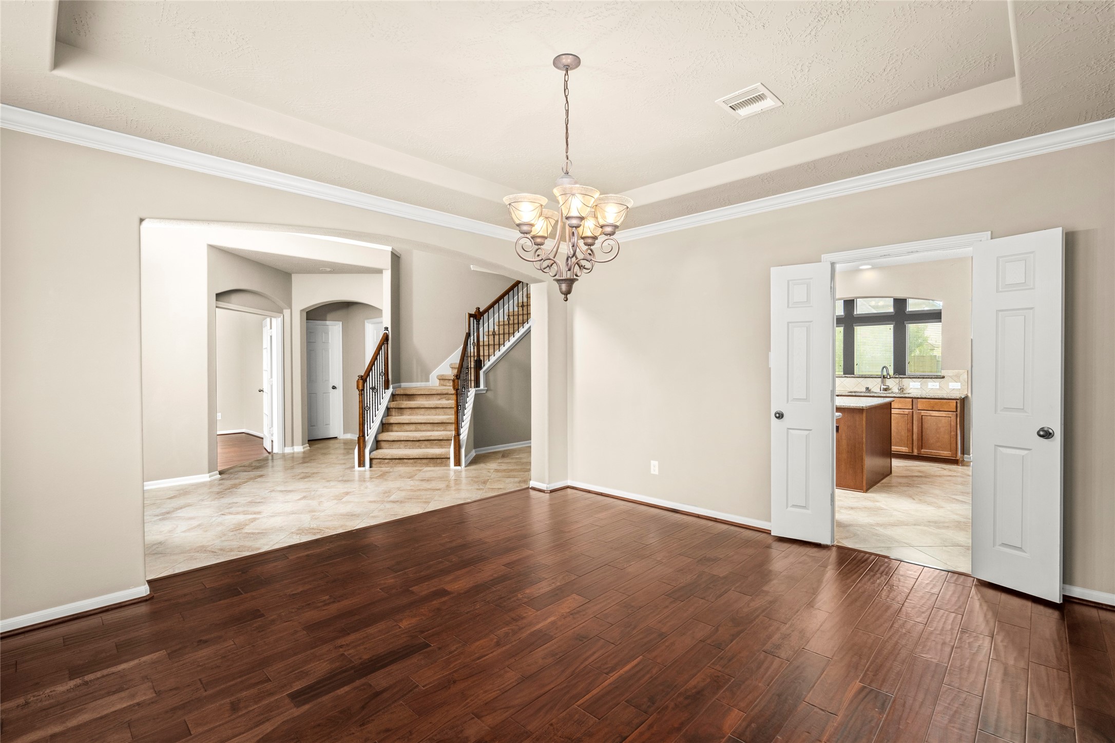 5307 Amber Sky Lane Rosharon, TX 77583 - Photo 11 of 50 A seamless transition of rich wood and tile flooring leads from the dining room toward the staircase and kitchen, illuminated by a striking chandelier. Luxury living, beautifully connected.