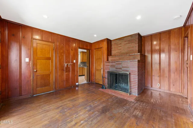 an empty room with wooden floor fireplace and windows