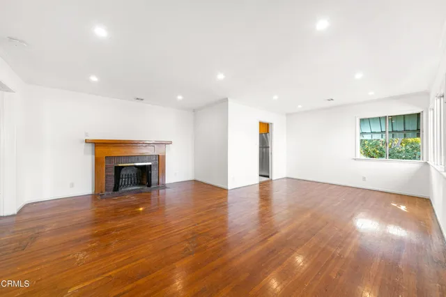 an empty room with wooden floor fireplace and windows
