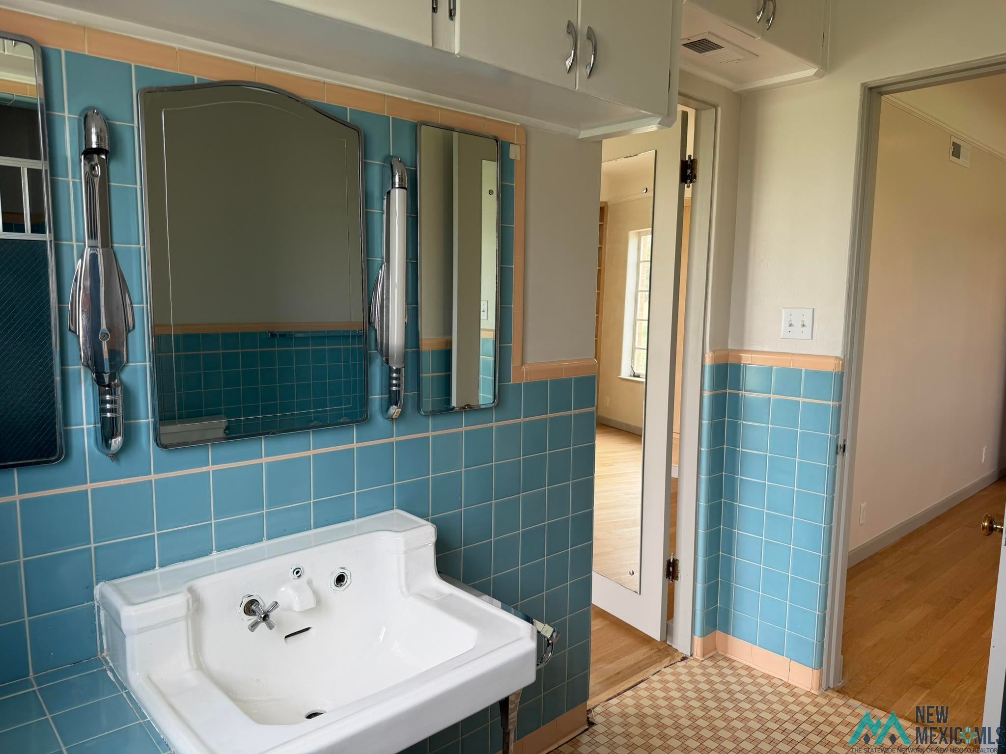 570 Curry Road North Clovis, NM 88101 - Photo 35 of 59 Bathroom featuring blue wall tile with peach accent trim, white wall-mounted sink, built-in medicine cabinet, and overhead cabinetry