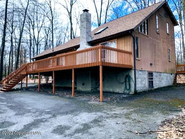 a view of a house with a yard and deck under a large tree