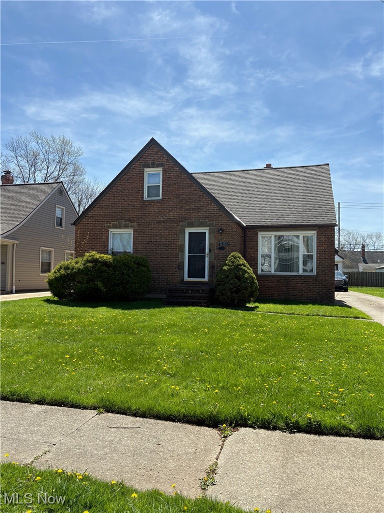 View of front of home featuring brick siding, a front yard, roof with shingles, and entry steps