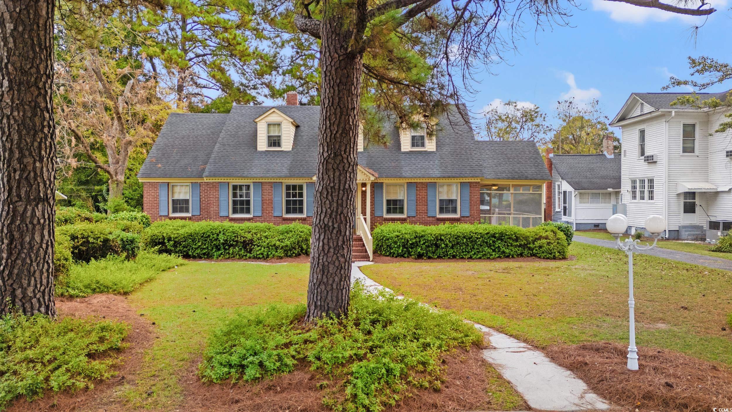 310 North Main Street Mullins, SC 29574 - Photo 4 of 35 Cape cod house with brick siding, a front lawn, a chimney, and a shingled roof