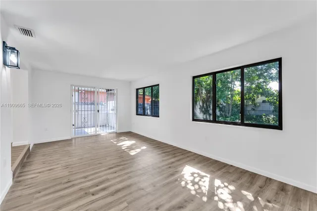 a view of an empty room with wooden floor and a window