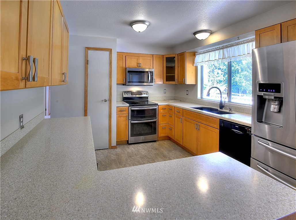 10020 Northeast 204th Street Bothell, WA 98011 - Photo 8 of 30 a kitchen with stainless steel appliances granite countertop a sink a stove top oven a refrigerator with grey cabinets and wooden floor