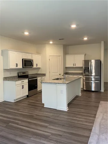 a large kitchen with stainless steel appliances granite countertop a stove top oven a refrigerator and white cabinets with wooden floor