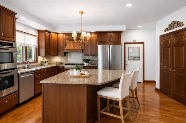 a kitchen with stainless steel appliances granite countertop a refrigerator a sink dishwasher a stove and a dining table with wooden floor