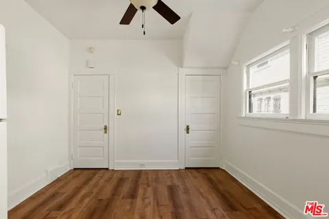 an empty room with wooden floor chandelier fan and windows
