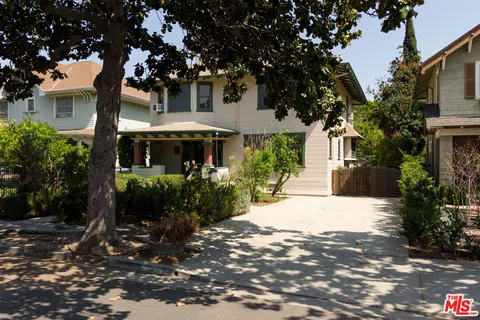 a view of a white house with a yard plants and large tree