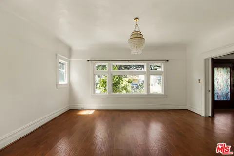 an empty room with wooden floor chandelier and windows