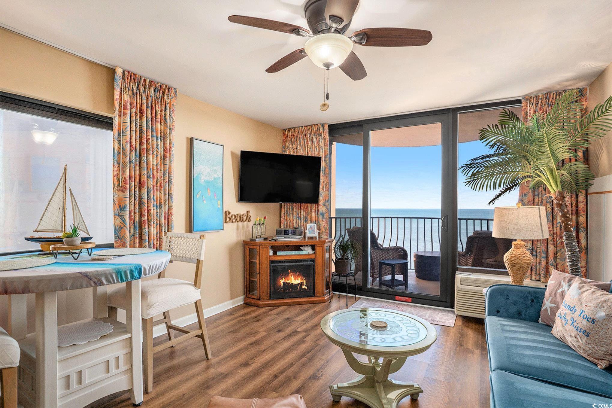 2406 North Ocean Boulevard, Unit 1203 Myrtle Beach, SC 29577 - Photo 3 of 24 Living room with wood finished floors, plenty of natural light, a wall of windows, a warm lit fireplace, and ceiling fan