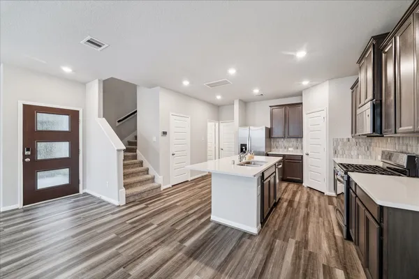 a kitchen with a sink stainless steel appliances counter space and wooden floor