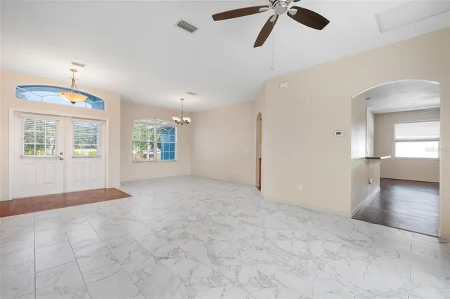 an empty room with chandelier fan and windows