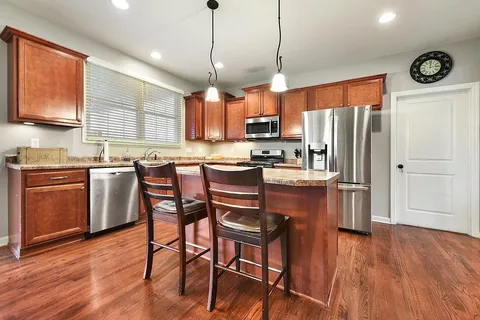 a kitchen with stainless steel appliances granite countertop wooden floors a stove a microwave a center island and a window