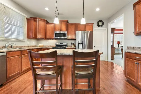 a kitchen with stainless steel appliances kitchen island granite countertop a refrigerator a stove a sink a dining table and chairs with wooden floor