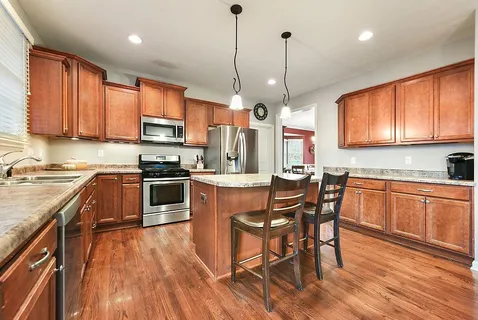 a kitchen with stainless steel appliances granite countertop wooden floor a stove a sink a refrigerator with a dining table and chairs