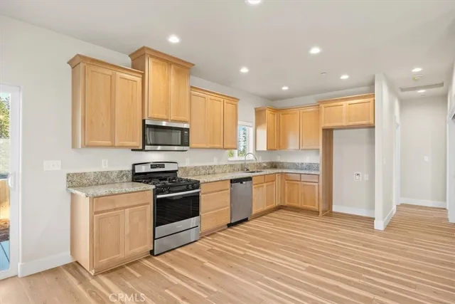 a kitchen with stainless steel appliances granite countertop a stove top oven a sink dishwasher and a refrigerator with wooden floor