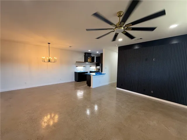 a view of an empty room with kitchen and a ceiling fan
