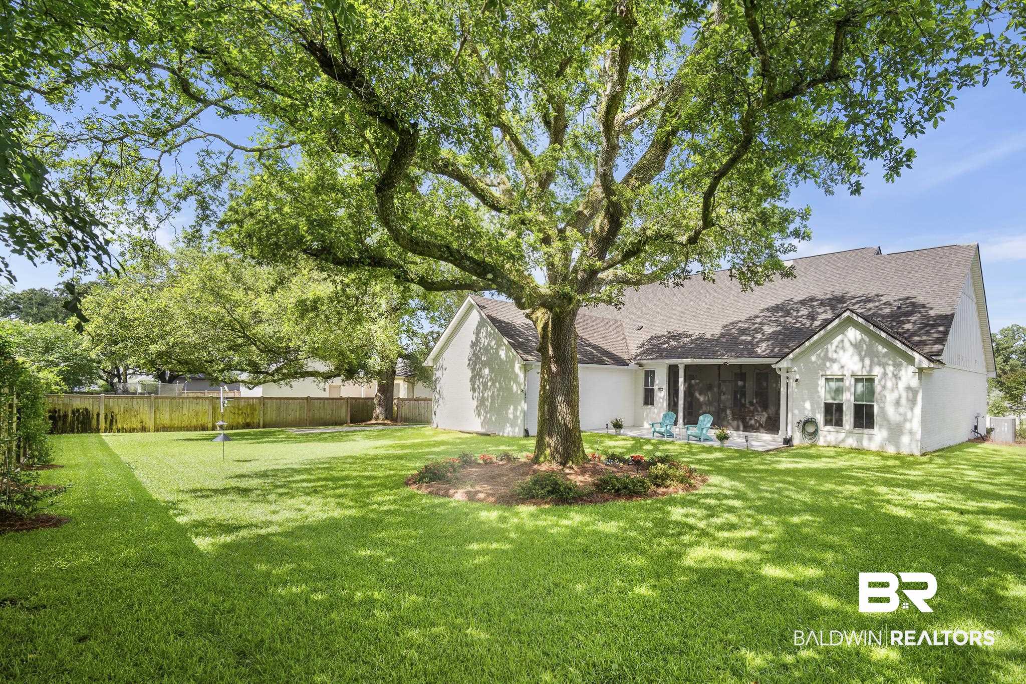 21702 Pillars Street Fairhope, AL 36532 - Photo 35 of 54 Expansive backyard featuring a mature shade tree, a white painted brick exterior, a screened patio, and a wood privacy fence