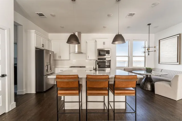 a kitchen with stainless steel appliances kitchen island granite countertop a refrigerator a stove a oven with white cabinets and wooden floor