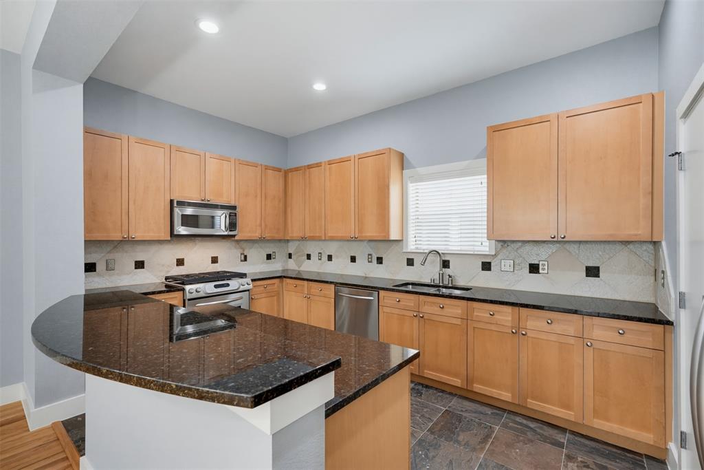 4830 Cedar Springs Road, Unit 30 Dallas, TX 75219 - Photo 10 of 32 Kitchen featuring a curved peninsula with a dark countertop, light wood cabinetry, a stainless steel microwave, a stainless steel range, and a stainless steel dishwasher
