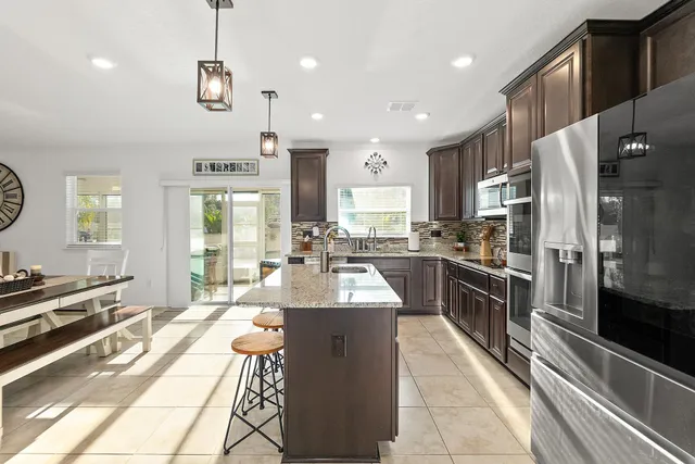 a large kitchen with stainless steel appliances kitchen island granite countertop a large counter top a stove a chimney a sink and a refrigerator