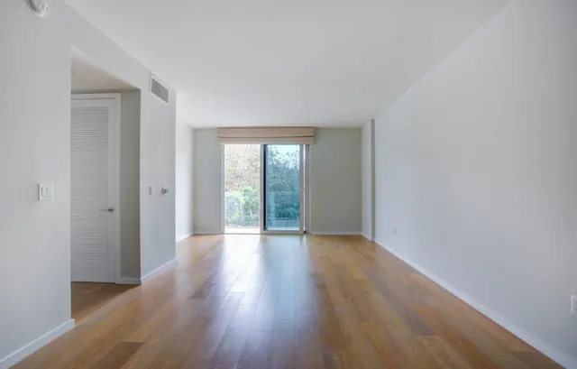 a view of an empty room with wooden floor and a window