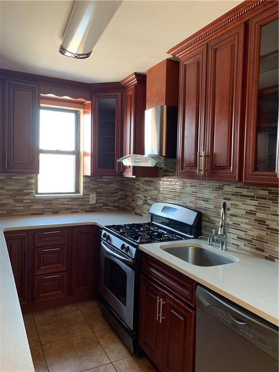 2564 Paulding Avenue Bronx, NY 10469 - Photo 2 of 14 Kitchen with stainless steel range with gas cooktop, wall chimney range hood, dishwasher, light countertops, and light tile patterned floors