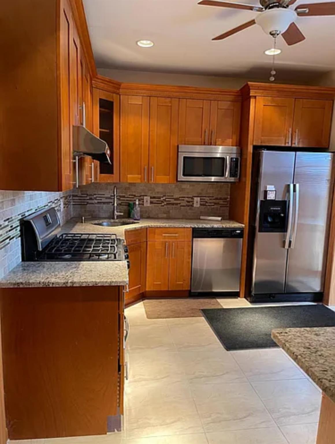 2564 Paulding Avenue Bronx, NY 10469 - Photo 5 of 14 Kitchen featuring stainless steel appliances, tasteful backsplash, ceiling fan, brown cabinetry, and under cabinet range hood