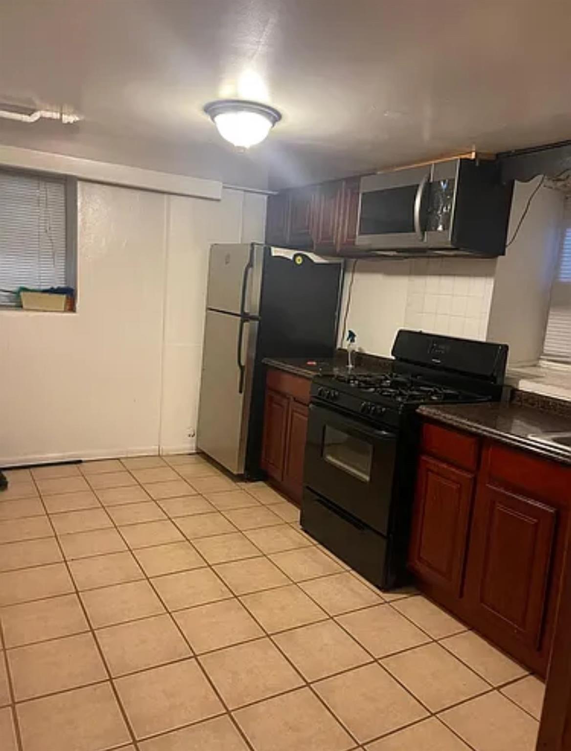 2564 Paulding Avenue Bronx, NY 10469 - Photo 10 of 14 Kitchen featuring black gas range oven, dark countertops, light tile patterned floors, stainless steel microwave, and freestanding refrigerator