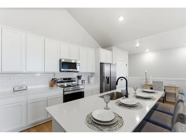 a kitchen with stainless steel appliances granite countertop a sink a stove a refrigerator with white cabinets and couches