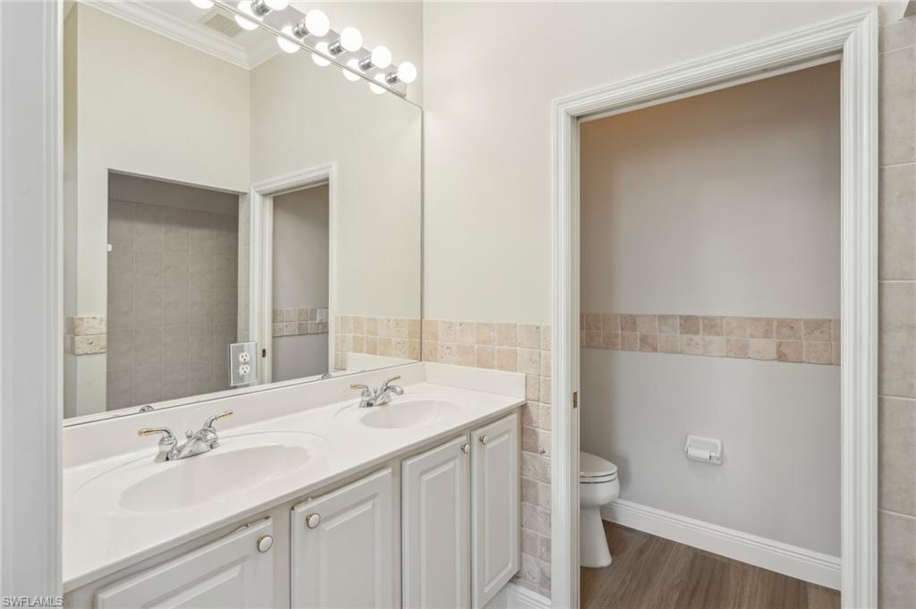 3653 Periwinkle Way Naples, FL 34114 - Photo 20 of 49 Full bathroom featuring double vanity, tile walls, dark wood-type flooring, and a wainscoted wall