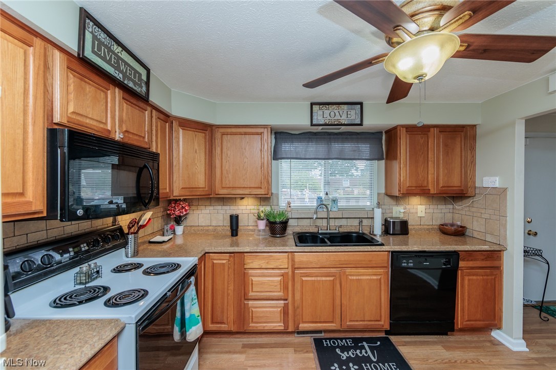 6476 State Road, Unit H8 Cleveland, OH 44134 - Photo 9 of 35 Kitchen with black appliances, brown cabinets, light countertops, light hardwood flooring, backsplash, and ceiling fan