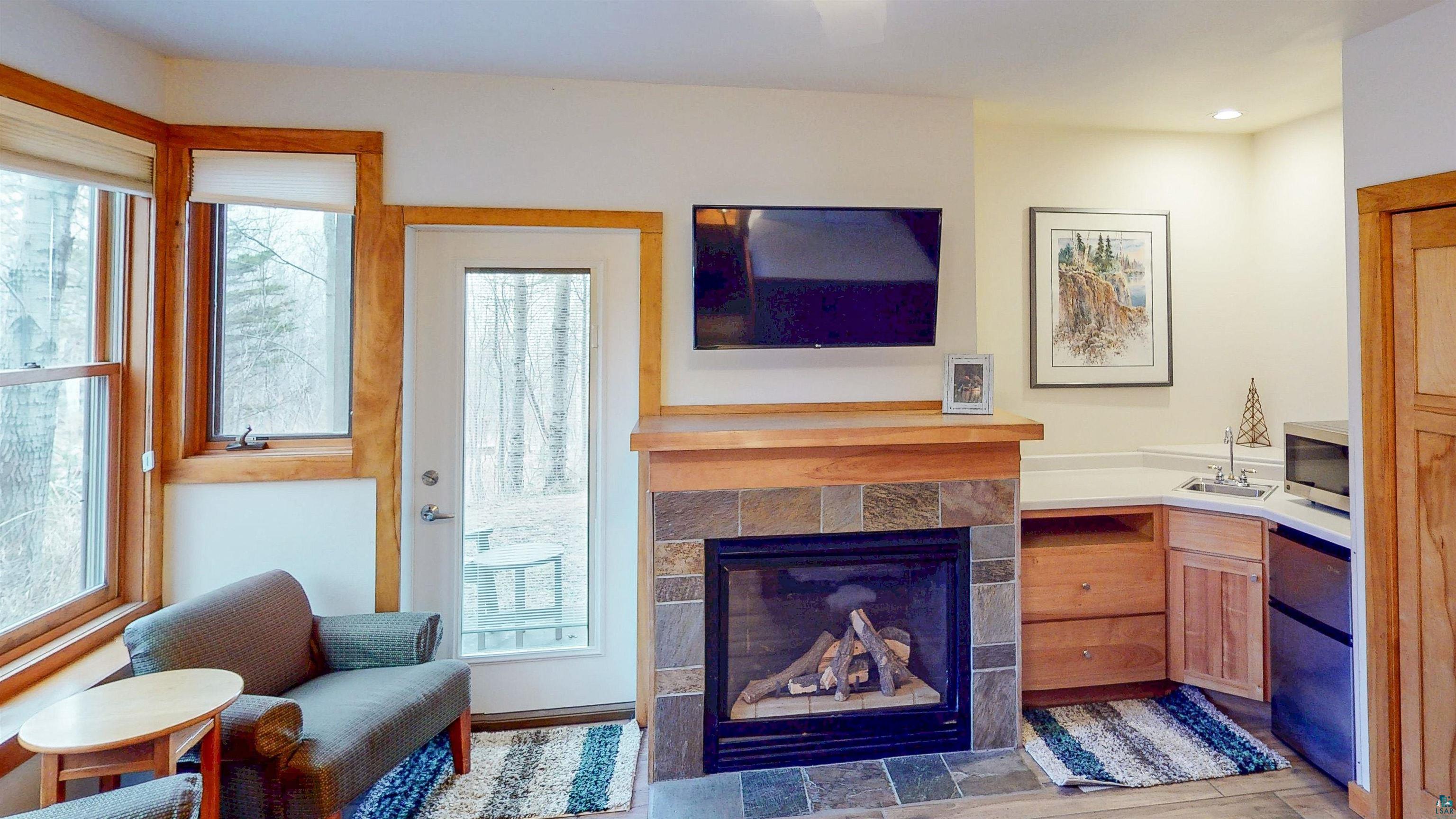 504-506 Poplar River Road, Unit 505 Lutsen, MN 55612 - Photo 19 of 39 Stone-faced fireplace with a wood mantle, corner wet bar featuring a built-in sink and countertop, and integrated under-counter refrigerator and microwave