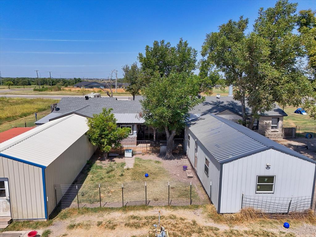 Main residence with a gray shingle roof, two outbuildings with metal roofs, and a fenced yard