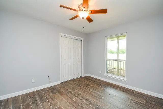 an empty room with wooden floor chandelier fan and windows