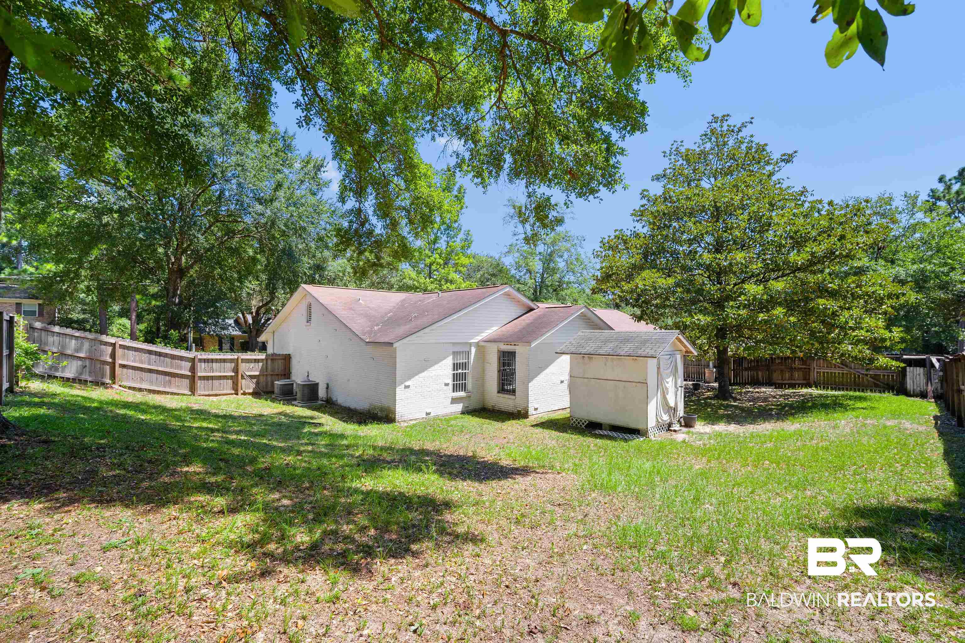 5559 Woodside Drive North Mobile, AL 36608 - Photo 2 of 28 Rear view of house featuring a fenced backyard, brick siding, a storage shed, and view of scattered trees
