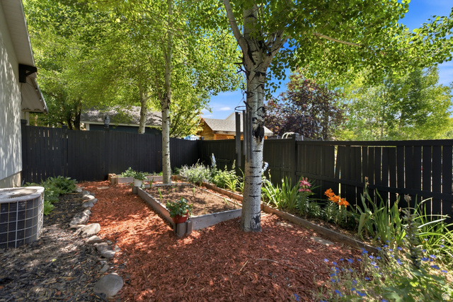 5196 Rodeo Circle Oakley, UT 84055 - Photo 54 of 57 Private backyard featuring a dark-toned privacy fence, mature trees providing shade, raised garden beds, wood chip ground cover, and various planted flowers