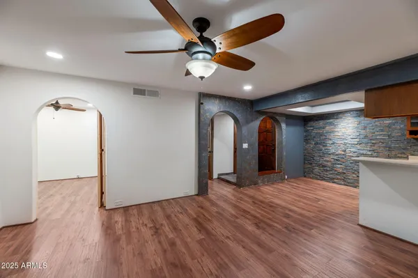 a view of an empty room with wooden floor and a ceiling fan