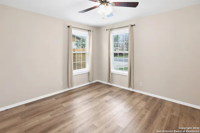 an empty room with wooden floor fan and windows