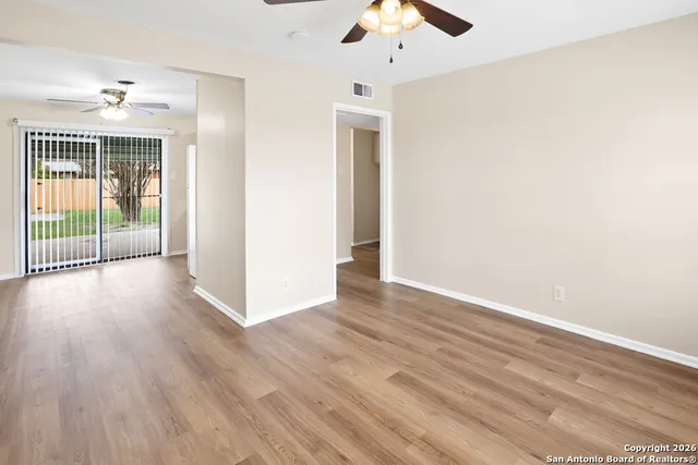 an empty room with wooden floor fan and windows