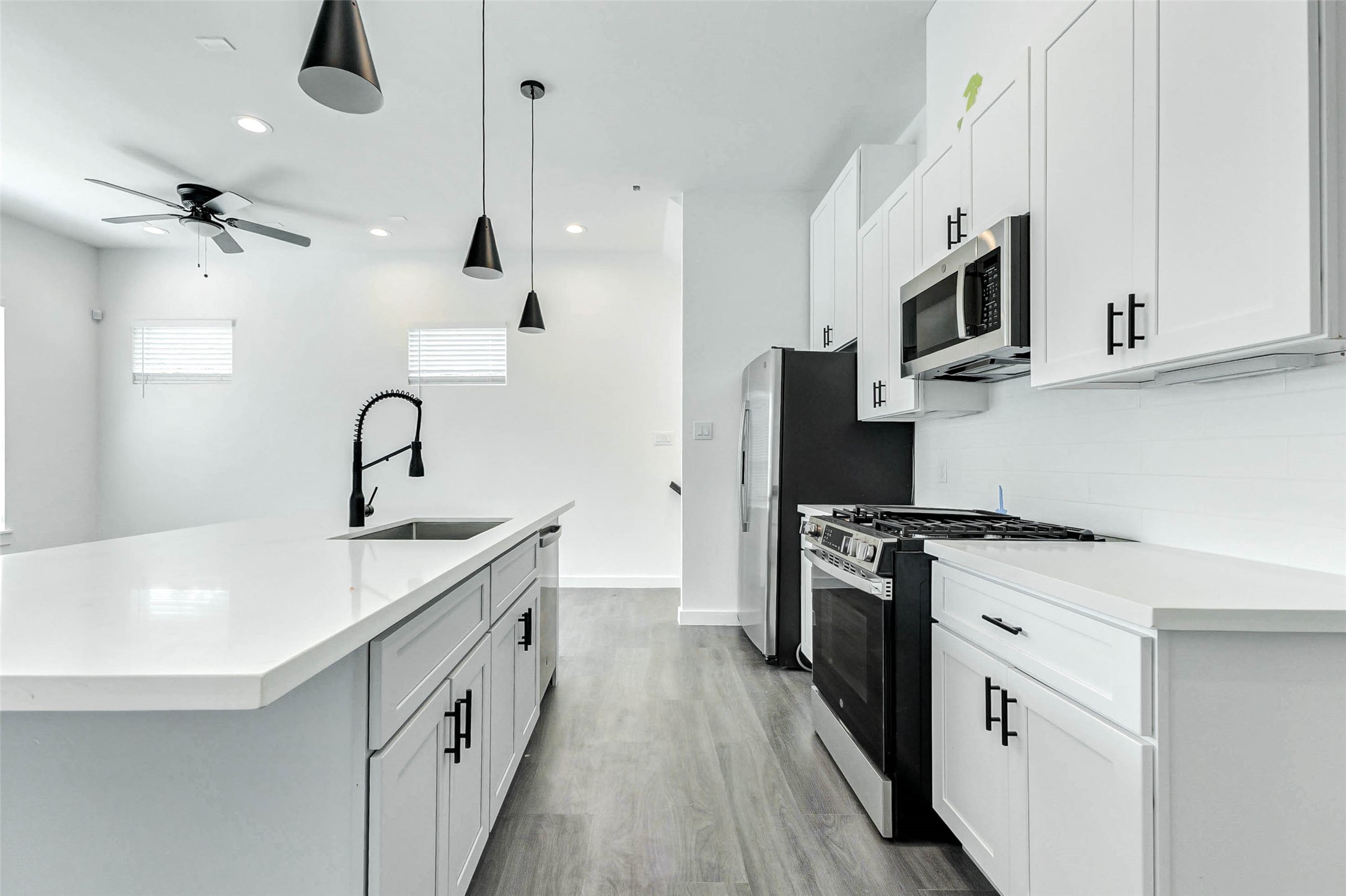 6013 Beall Street Houston, TX 77091 - Photo 5 of 26 Clean lines and designer finishes shine in this modern kitchen, featuring a gooseneck pull-down faucet, pendant lighting, quartz countertops, and stainless appliances all centered around a large island with seating space.