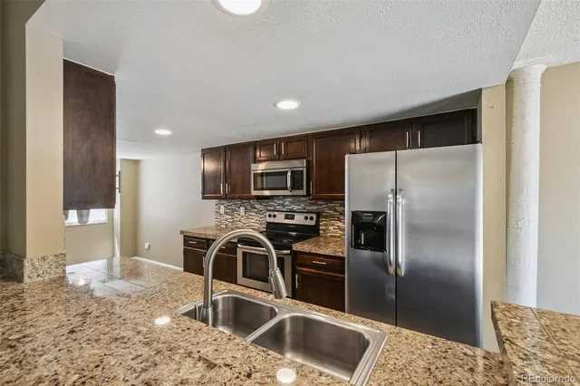 a kitchen with stainless steel appliances granite countertop a refrigerator a stove and a sink