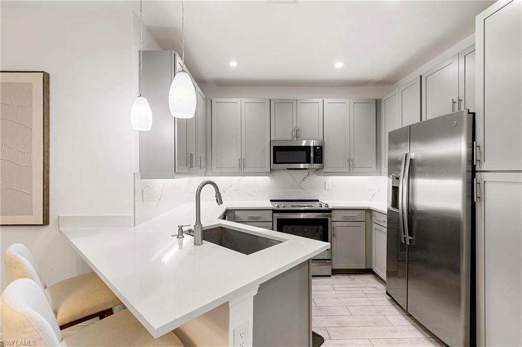 7622 Rockefeller Drive Naples, FL 34119 - Photo 4 of 35 a kitchen with stainless steel appliances a sink a stove a refrigerator with white cabinets and wooden floor