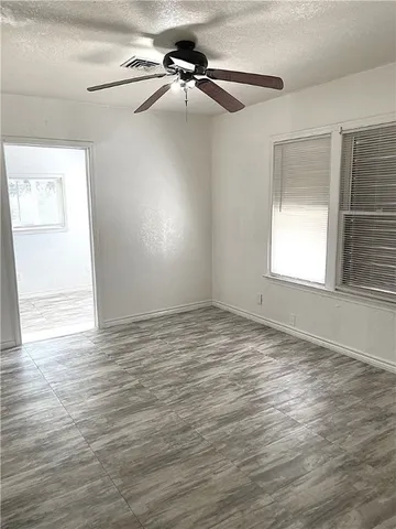 an empty room with wooden floor fan and windows