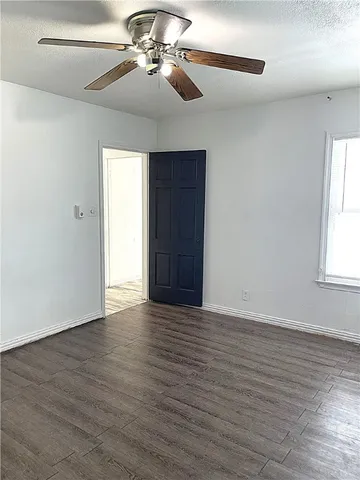 an empty room with wooden floor chandelier fan and windows