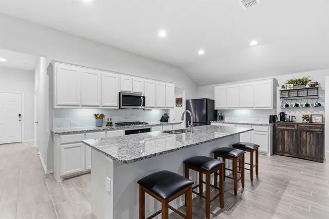 a kitchen with stainless steel appliances granite countertop a stove top oven a sink dishwasher a refrigerator and white cabinets with wooden floor