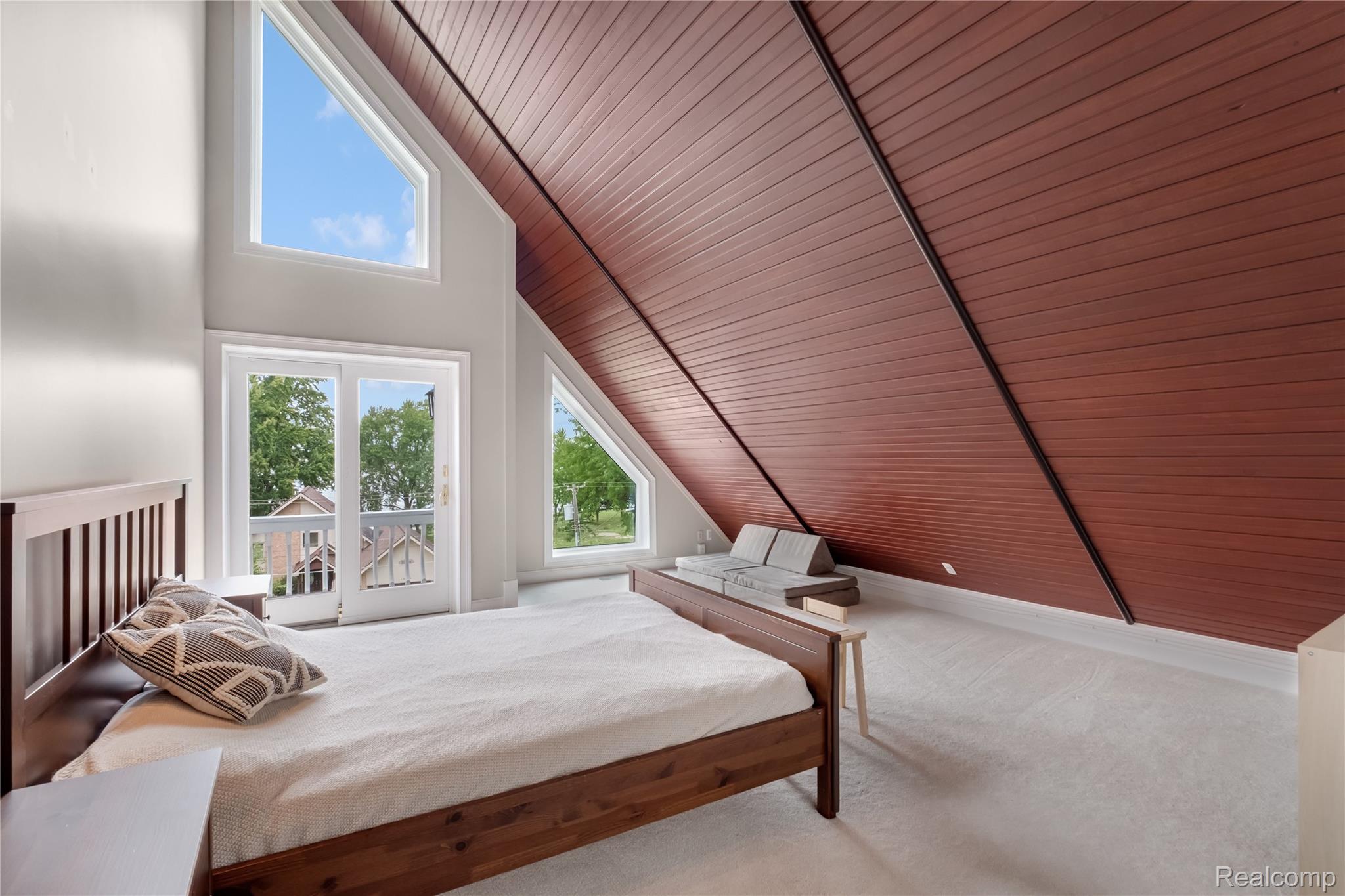 15420 Jennings Road Fenton, MI 48430 - Photo 21 of 45 Bright attic bedroom with vaulted wood-finish ceiling, angled architectural lines, and abundant natural light from multiple windows overlooking mature landscaping