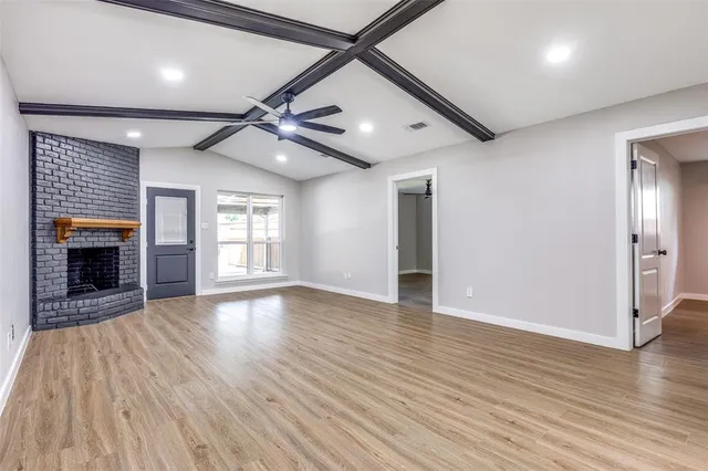 a view of an empty room with wooden floor fireplace and a window